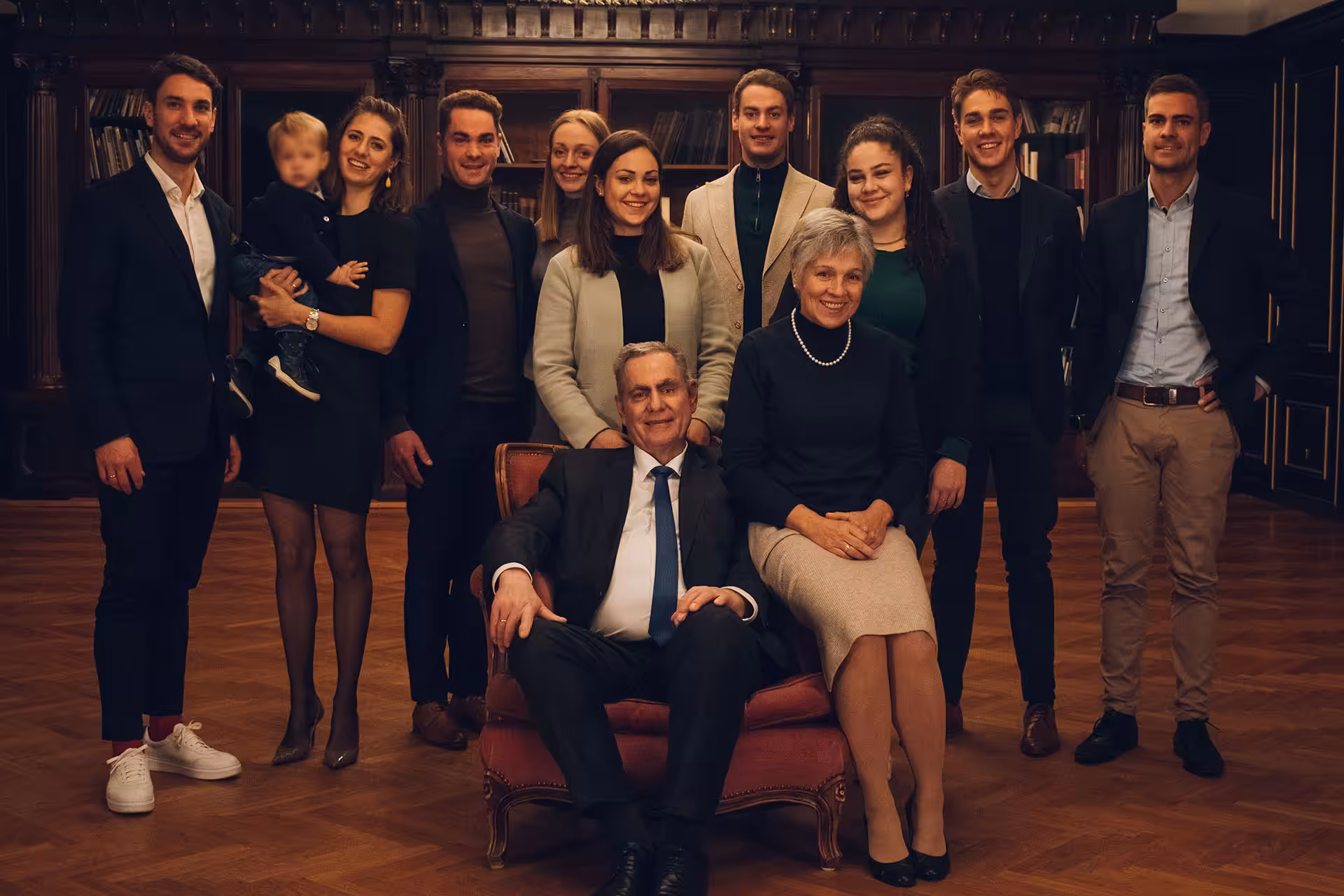 Die Bauer-Familie und das Halleluja Sauna®-Team in eleganter Bibliothek mit rotem Sessel und Kristallleuchter.